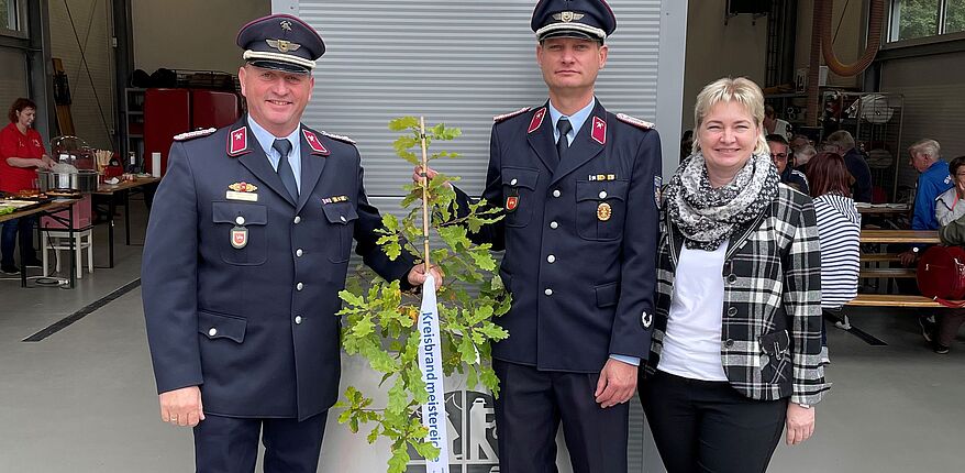 Vor den beiden Toreinfahren des Feuerwehrgerätehauses in Rottmersleben haben Kreisbrandmeister Matthias Schumann, Ortswehrleiter Thomas Brzezinski und Amtleiterin Corinna Sladky Aufstellung zum Erinnerungsfoto genommen. Der Kreisbrandmeister überreicht einen "Eichensetzling".