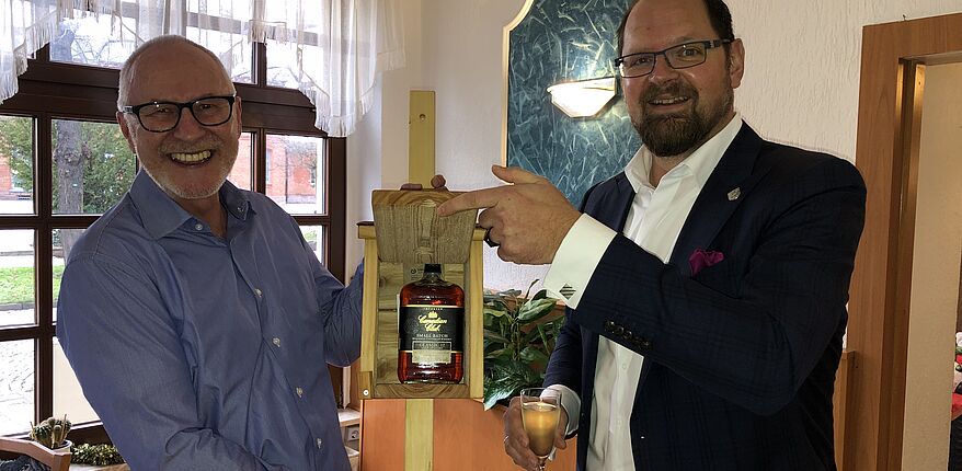 Das Foto zeigt Landrat Martin Stichnoth und Frank Schulze. Stichnoth überreicht sein Abschiedsgeschenk, ein Vogelhaus, darin eine Flasche Whisky. 