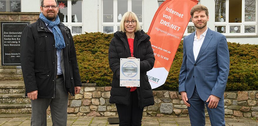 DAs Foto zeigt 3 Personen vor der Förderschule in Klein Oschersleben, von links nach rechts Landrat martin Stichnoth, Schulleiterin Silke Heick mit dem Zertifikat in den Händen und Widar Wendt (atene-kom).