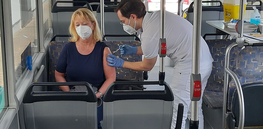 Das Foto zeigt einen Einblick in das "Innere" eines Impfbusses. Ein impfberechitgte Person nimmt im Bild die Impfung vor 