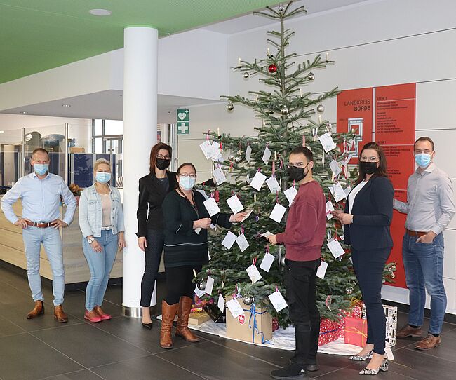 Das Foto im Foyer der Kreisverwaltung in Haldensleben zeigt einen auch mit Wunschzetteln geschmückten Weihnachtsbaum. Davor mehrere Beschäftigte der Kreisverwaltung, die Wunschzettel abnehmen, um Wünsche von Kindern zu Weihnachten zu erfüllen. 