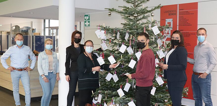 Das Foto im Foyer der Kreisverwaltung in Haldensleben zeigt einen auch mit Wunschzetteln geschmückten Weihnachtsbaum. Davor mehrere Beschäftigte der Kreisverwaltung, die Wunschzettel abnehmen, um Wünsche von Kindern zu Weihnachten zu erfüllen. 