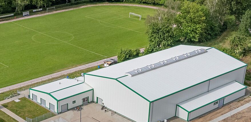 Foto TSV Hadmersleben / auch Landrat Martin Stichnoth war zur Eröffnung da / mehr Fotos über Instagram (Landkreis Börde) verfügbar. auf dem Bild sieht man die Sporthalle aus der Vogelperspektive, dahinter der Außensportplatz.
