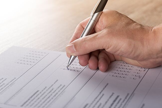 Das Foto (Symbolbild / Pixabay-Andreas Breitling) zeigt eine schreibende Hand auf einem Fragebogen