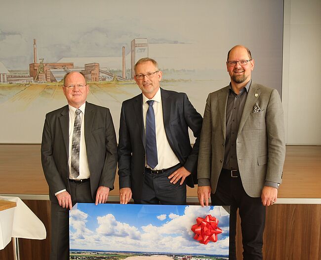 Foto Thorsten Kowalowka (Kaliwerk Zielitz) Landrat Martin Stichnoth und Thomas Webel verabschieden Dr. Holger Hoppe nach Kassel. Die drei stehen mit einem Bild von der Kalihalde als Abschiedsgeschenk nebeneineander.