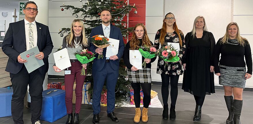 Foto Uwe Baumgart / Aufstellung zum Erinnerungsfoto (v.l.n.r.) Beigeordneter Dr. Marcus Waselewski, Laura Patermann, Leon Gäde, Hannah Pientka, Kimberly Könnecke, Personalchefin Julia Herzberg-Ebeling und Ausbildungsleiterin Manuela Brasch. Hintergrund, ein Weihnachtsbaum.