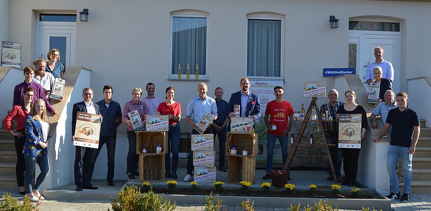 Das Foto mit 20 Personen, darunter Landrat Martin Stichnoth, ist auf dem Hof von Obstbauer Marcus Nickel in Hötensleben entstanden. Auf 2 Teppen zeigen die Direktvermarkter vor einem Gebäude die "Börde Schatz Kiste" und darauf hinweisende Werbematerialien