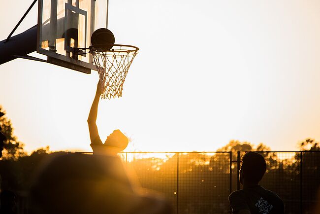 Basketball spielender Jugendlicher im Sonnenuntergang