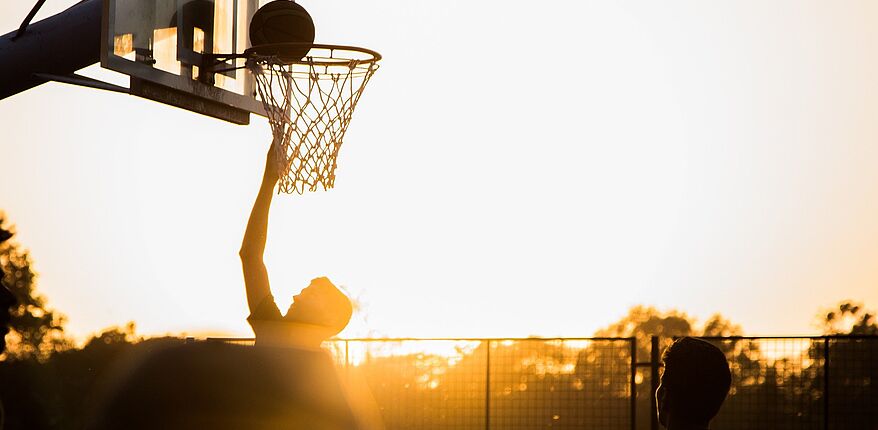 Basketball spielender Jugendlicher im Sonnenuntergang