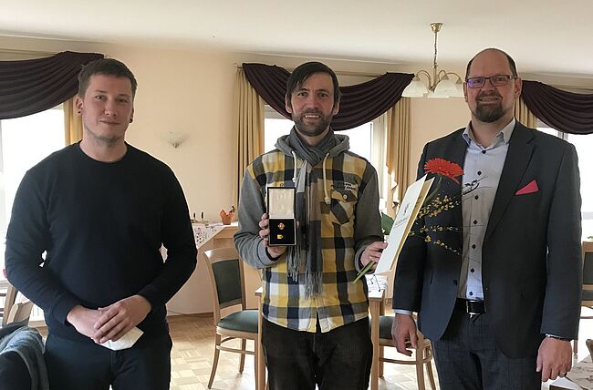 Foto Juliane Herm / Landrat Martin Stichnoth und der Landtagsabgeordnete Tim Teßmann zeichnen Ruben Herm mit der Ehrennadel des Landes Sachsen-Anhalt aus. Herm steht zwischen den beiden Herren. Er hat die Nadel und die Urkunde in den Händen. 