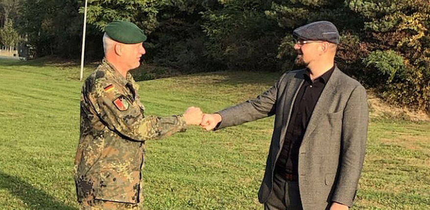 Das Foto zeigt Landrat Martin Stichnoth und Oberst Michael Knoke bei der Gratualtion in Letzlingen. Beide Herren begrüßen sich mit der "Faust". Sie stehen auf einer Wiese. Im Hintergrund ist ein Wald zu sehen. 