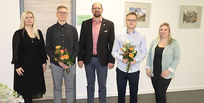 Uwe Baumgart / Landrat Martin Stichnoth, Personalamtsleiterin Julia Herzberg-Ebeling (links) und Ausbildungsleiterin Manuela Brasch (rechts) gratulieren Jannik Gläsmann (links neben dem Landrat) und Tobias Schenke zum Abschuss. Die Absolventen haben Blumensträuße in den Händen. 