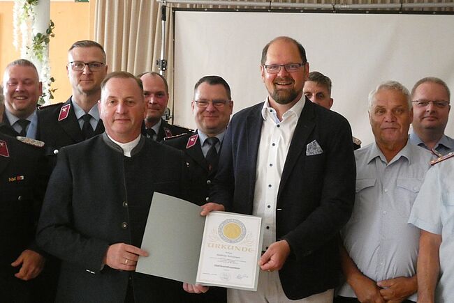 Foto Landkreis Börde / Kreisbrandsmeister Matthias Schumann hat nun den Dienstgrad "Oberbrandinspektor". Im Kreise mehrere Kameraden stehen Schuhmann und Stichnoth mit der Beförderungsurkunde in den Händen in der Mitte.